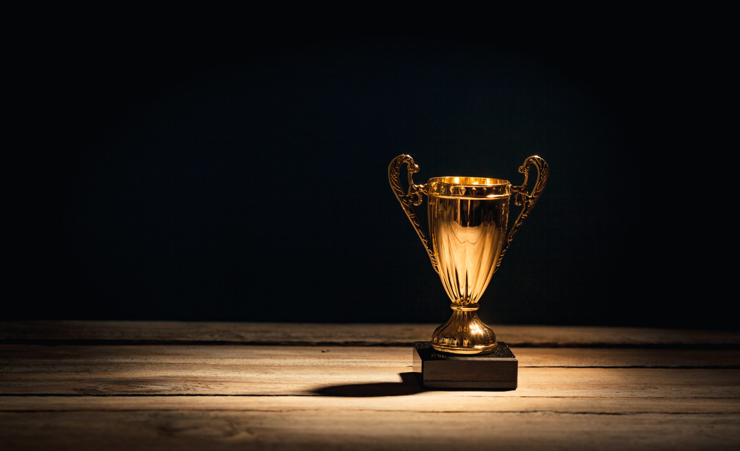 Golden sports trophy cup on wood desk with dramatic strong contrast light and shadow