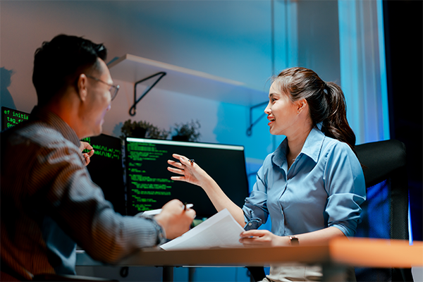 a women speaks with man and points at a computer screen with software code